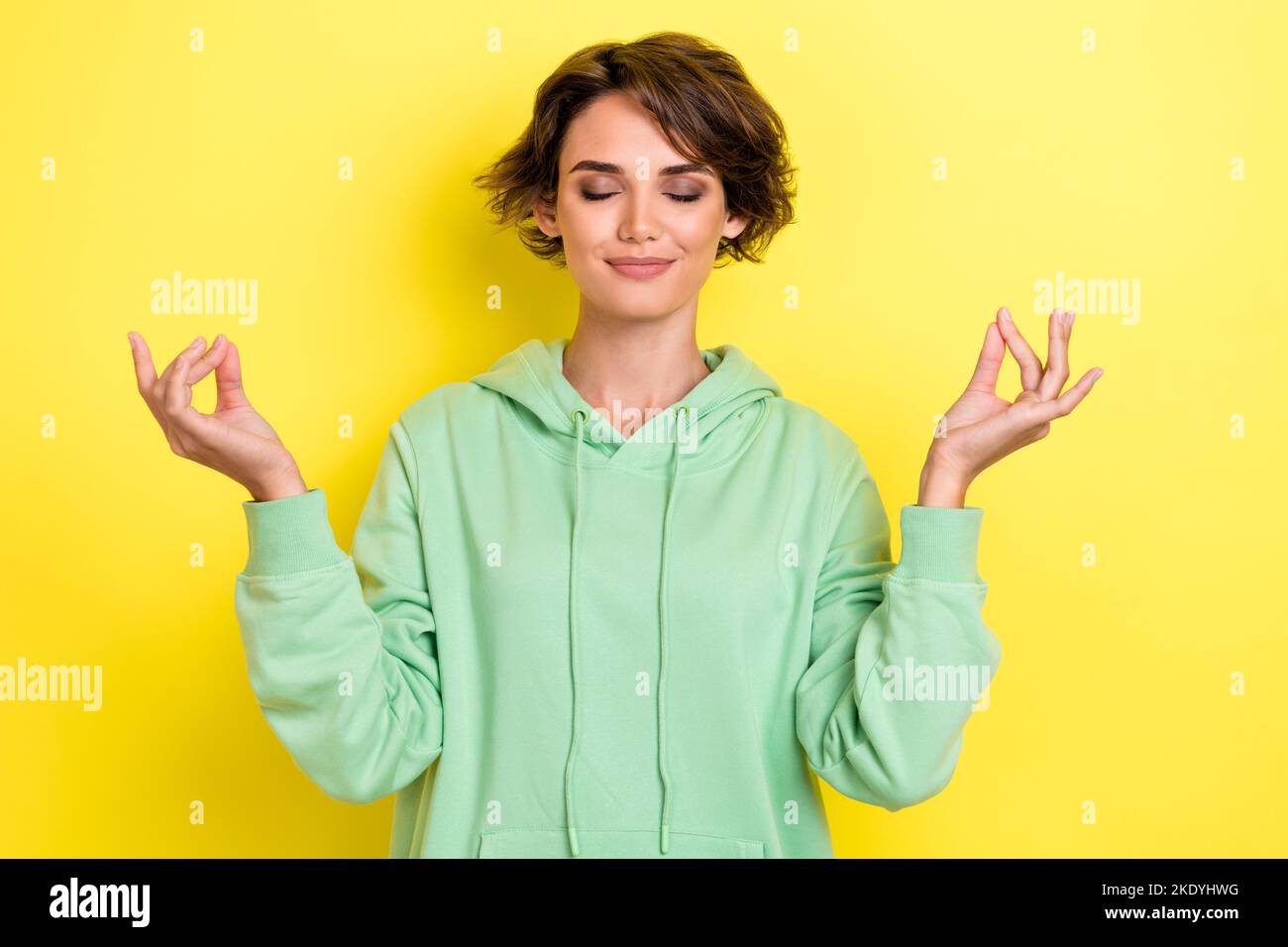 Ritratto fotografico di bella giovane donna occhi chiusi praticando meditazione tranquilla indossare abbigliamento trendy verde isolato su sfondo di colore giallo Foto Stock