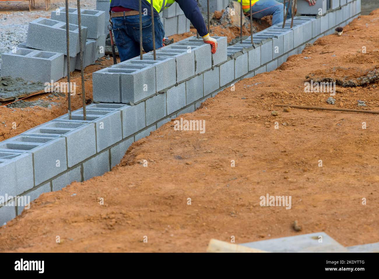 Lavoratore che mette blocchi di cemento lungo un'altra fila di mattoni in muratura cantiere Foto Stock