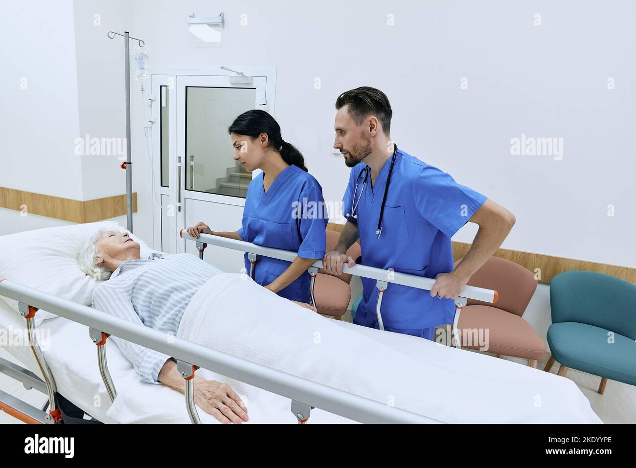 Due infermiere che sostengono la donna anziana sdraiata su una barella medica nella sala dell'ospedale con flebo IV. cura dei pazienti in ospedale Foto Stock