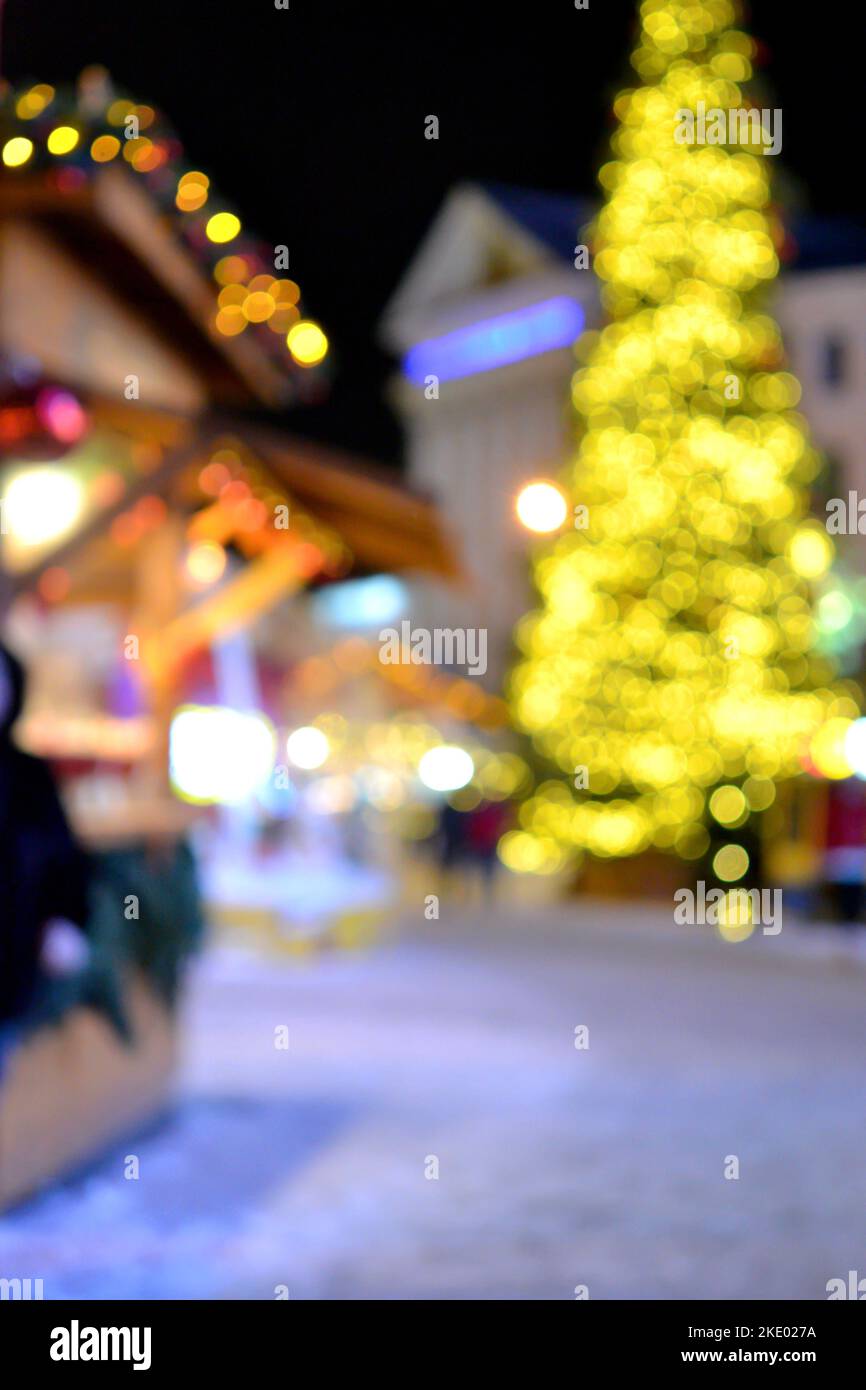 Sfondo sfocato. Albero di Natale di Capodanno decorato giallo ghirlande illuminazione, piccole case di legno ghirlande sul tetto e sagome di persone che camminano lungo la strada della città. Foto Stock