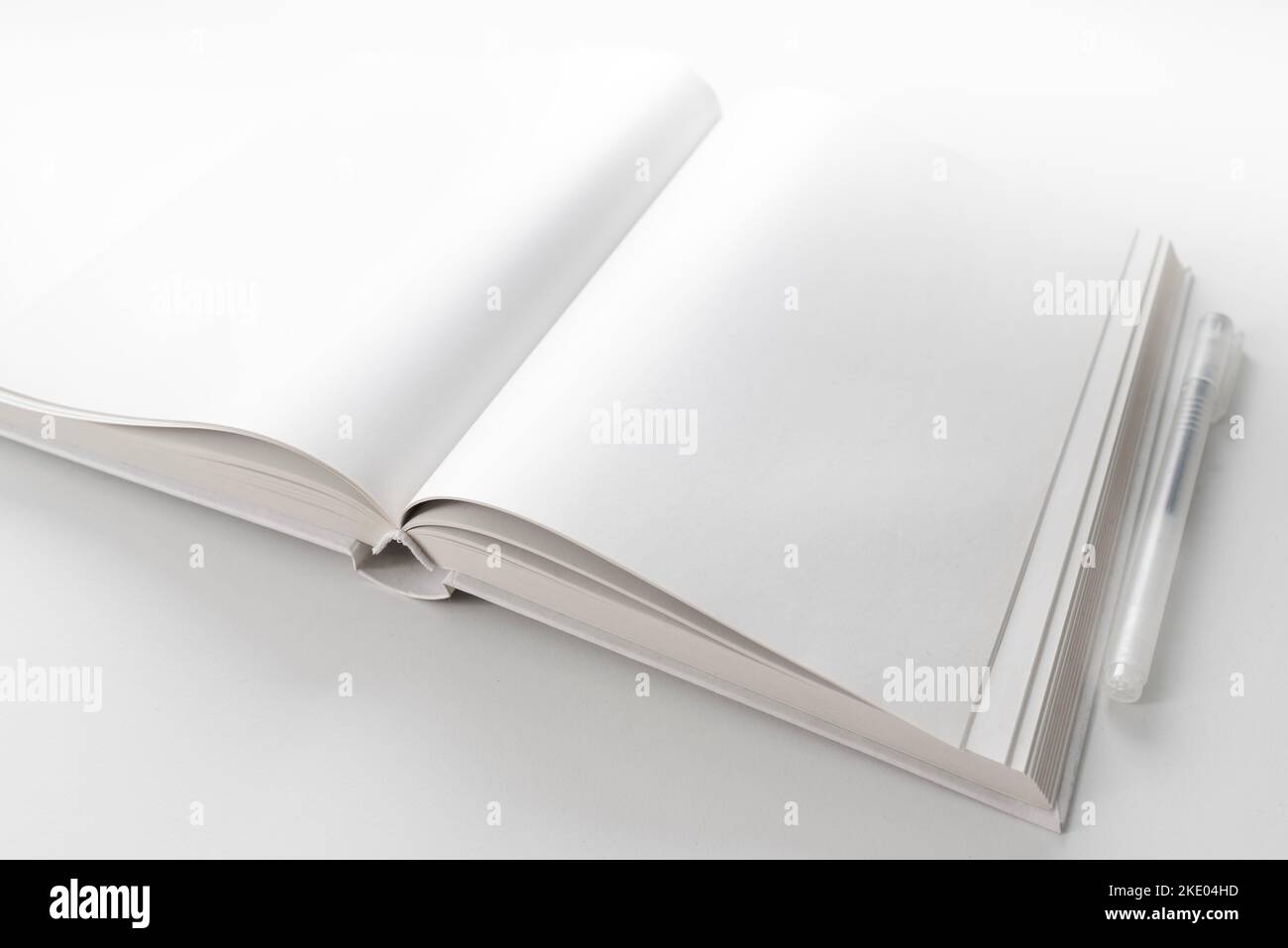 vista ad angolo alto di un libro aperto con pagine bianche bianche su una scrivania bianca con penna Foto Stock