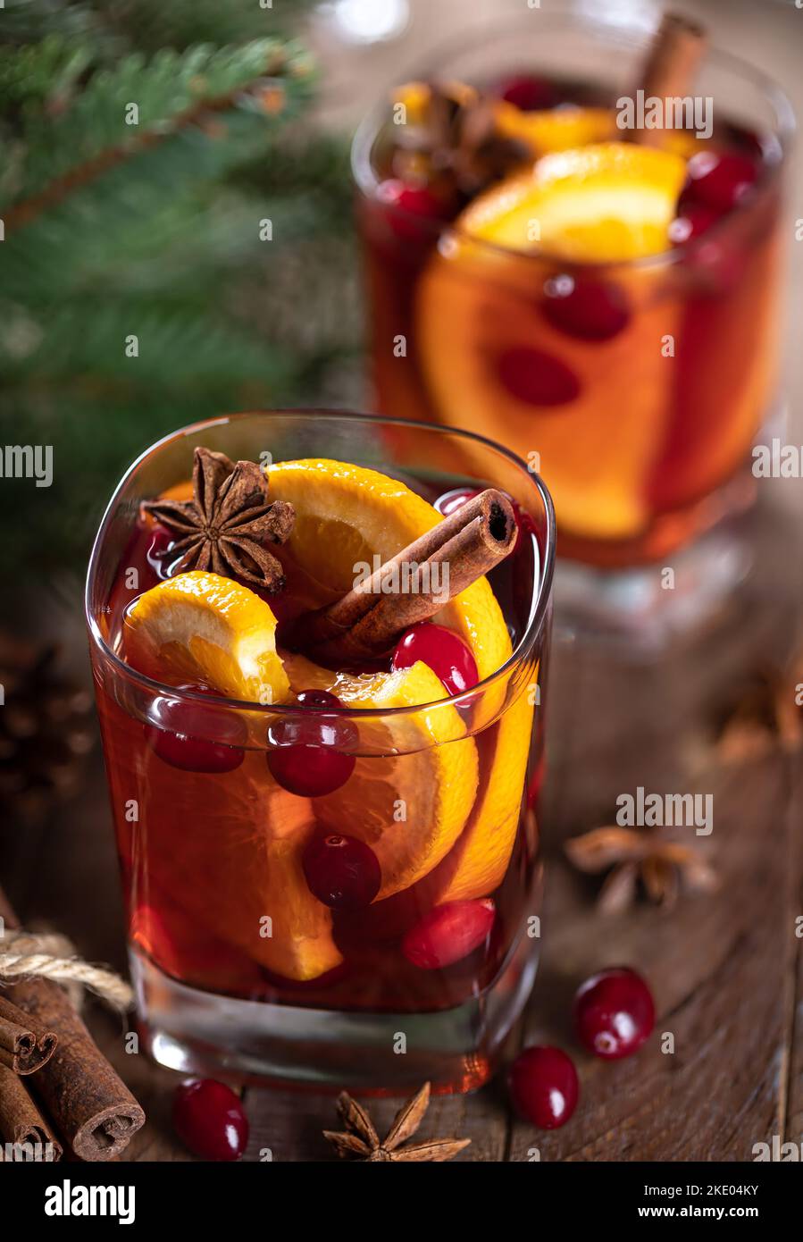 VIN brulé con fettine d'arancia, mirtilli rossi e spezie su un rustico tavolo di legno con decorazione dell'albero di Natale sullo sfondo Foto Stock