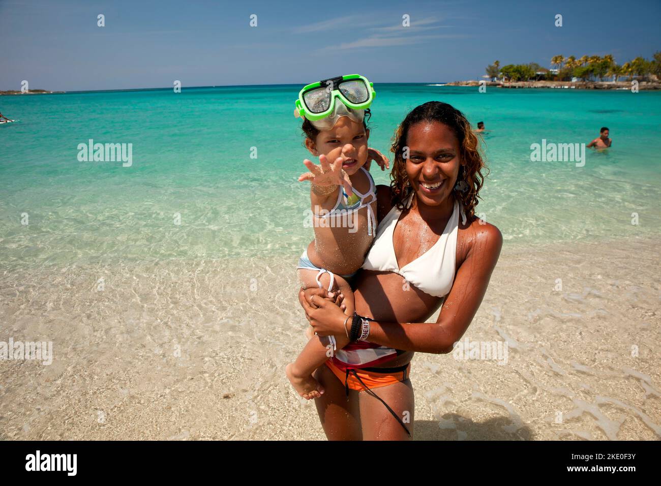 Froehliche junge Kubanerin mit kleinem Maedchen auf dem Arm am Strand von Bacuranao, Playas del este, Havanna, Kuba, Karibik | giovane coppia cubana sorridente Foto Stock