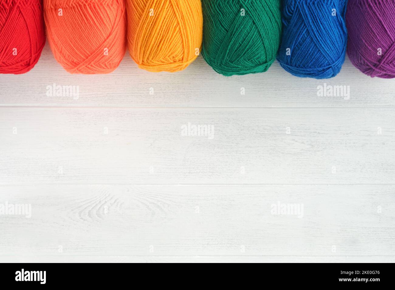 Molte palle multicolore di fili su tessuto lavorato a maglia su sfondi di legno bianco. Filati di fiori colorati, di maglieria e di crostini. Ago Foto Stock