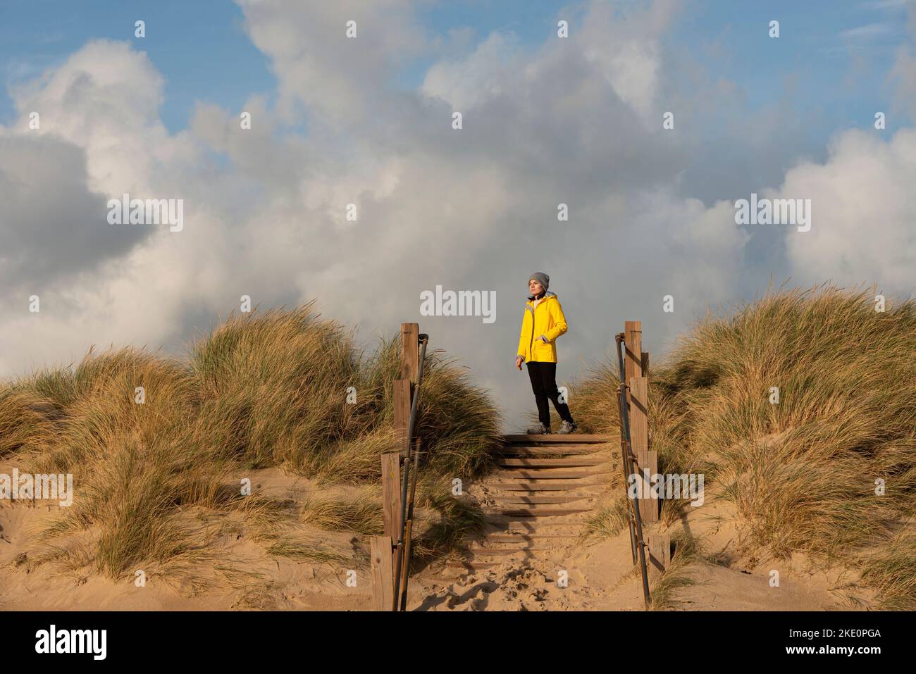 Donna che indossa un cappotto giallo in piedi in cima a dune di sabbia, guardando la vista. Foto Stock