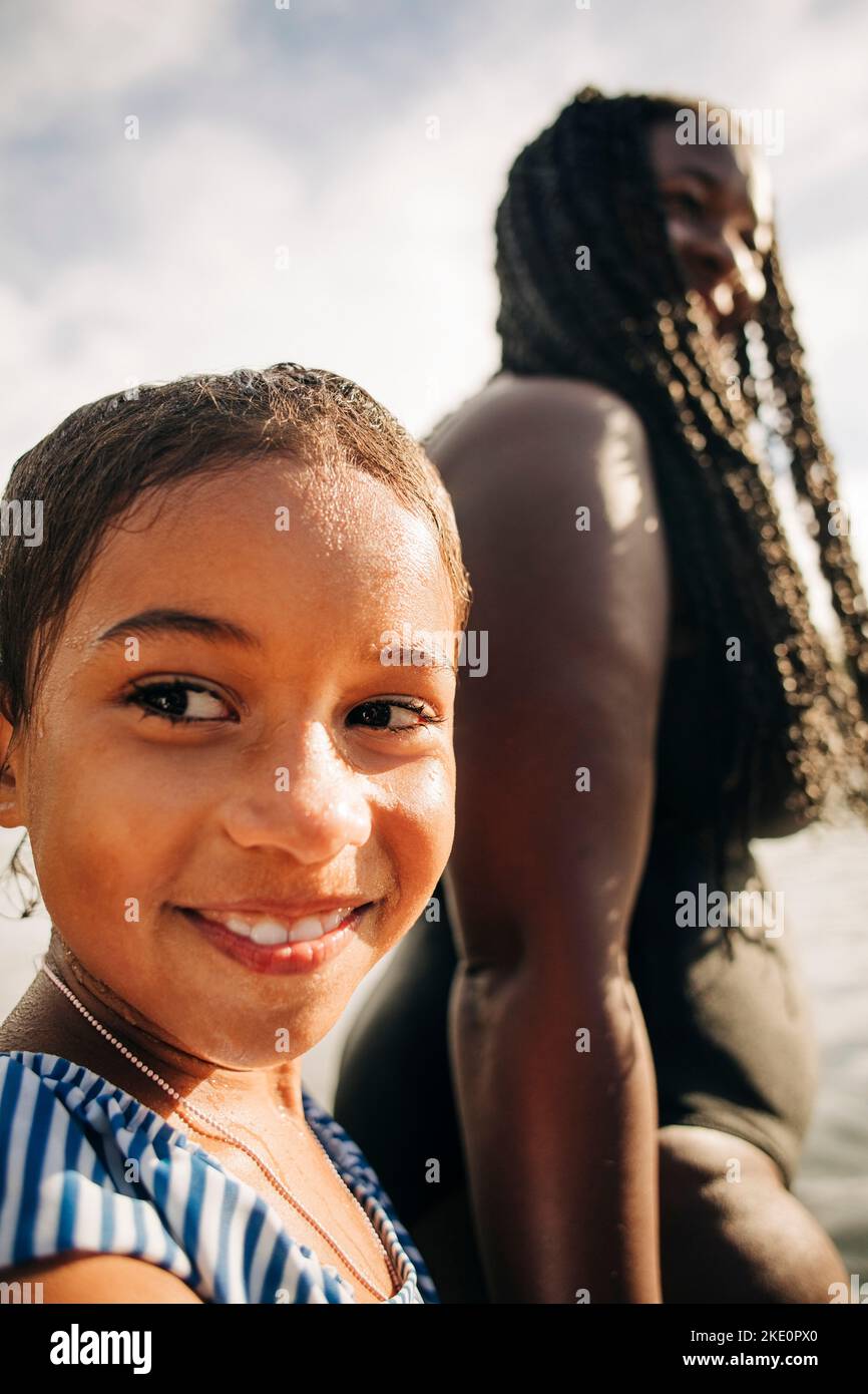 Ragazza sorridente che guarda via con la madre il giorno di sole Foto Stock