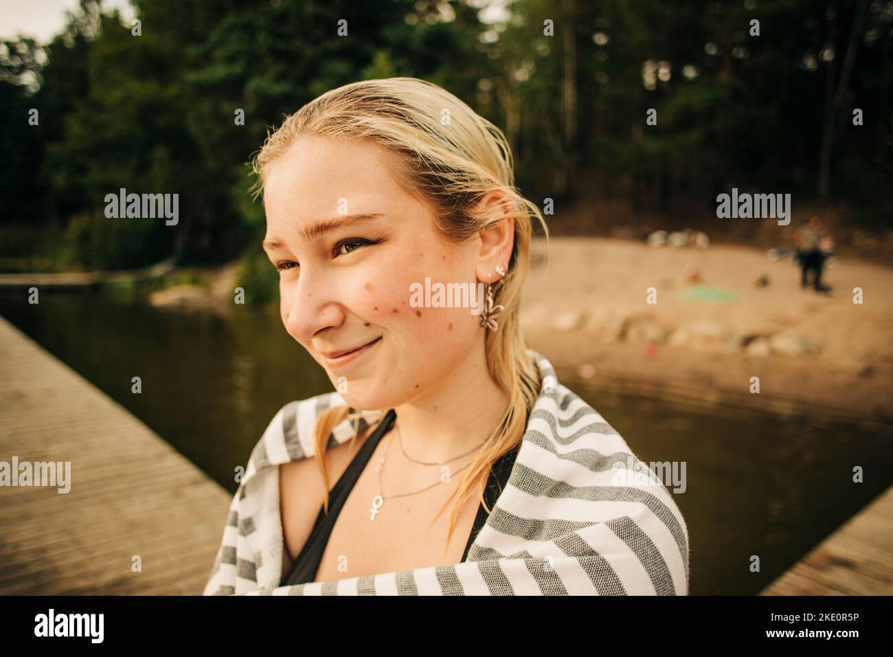 Donna bionda sorridente che indossa un asciugamano al lago durante le vacanze Foto Stock