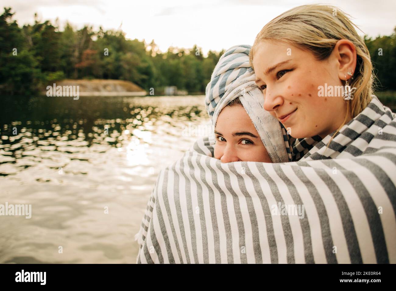 Donna che abbraccia l'amico femminile avvolto in asciugamano al lago durante le vacanze Foto Stock