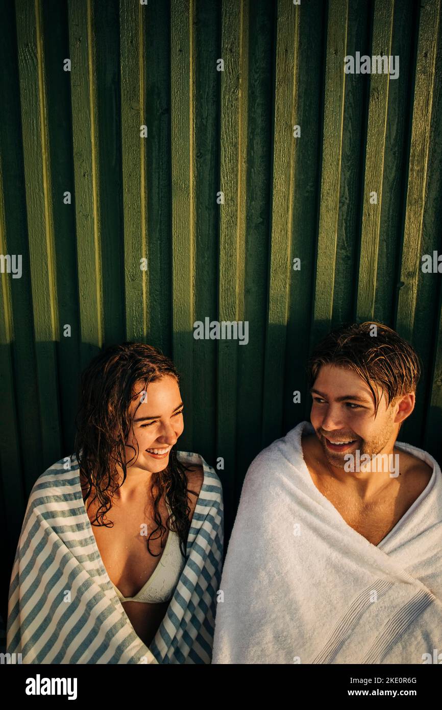 Sorridente uomo e donna che indossano un asciugamano mentre si parlano tra loro durante il tramonto Foto Stock