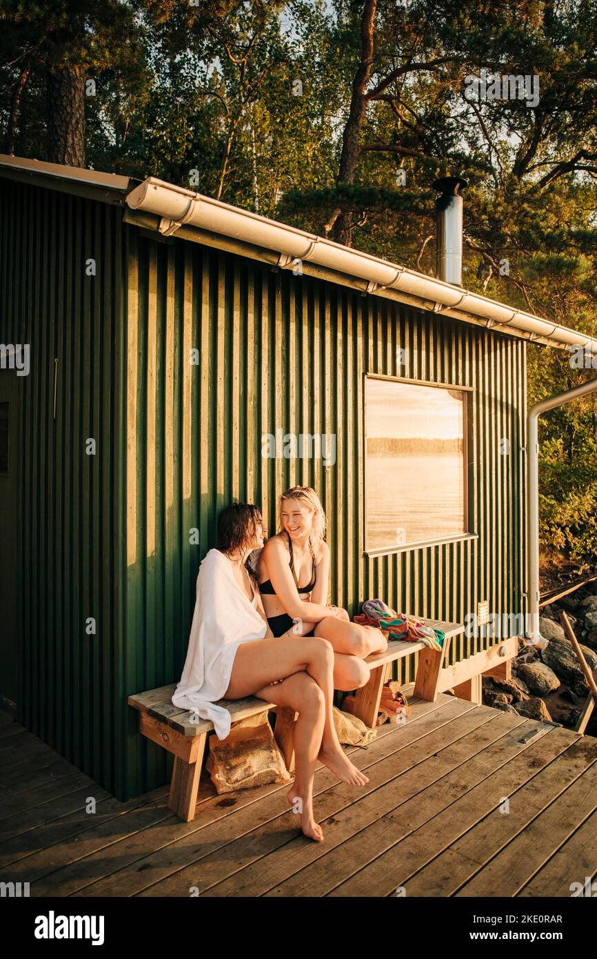 Amici femminili seduti sulla panca vicino al cottage durante il tramonto Foto Stock