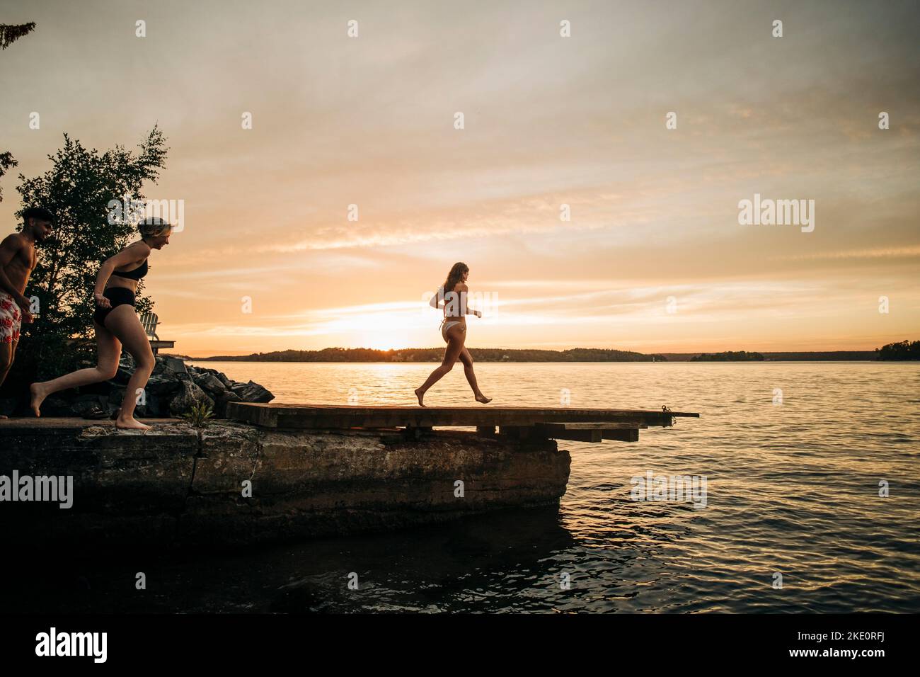 Amici che corrono sul molo verso il lago durante le vacanze al tramonto Foto Stock