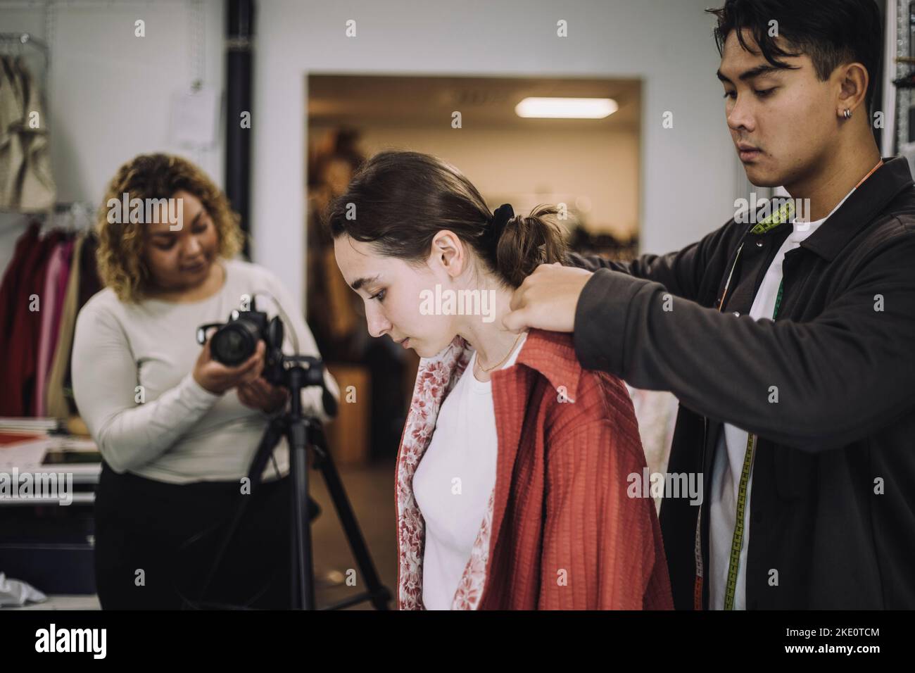 Design maschile che regola il colletto della camicia vicino alla modella femminile durante le riprese fotografiche in studio Foto Stock