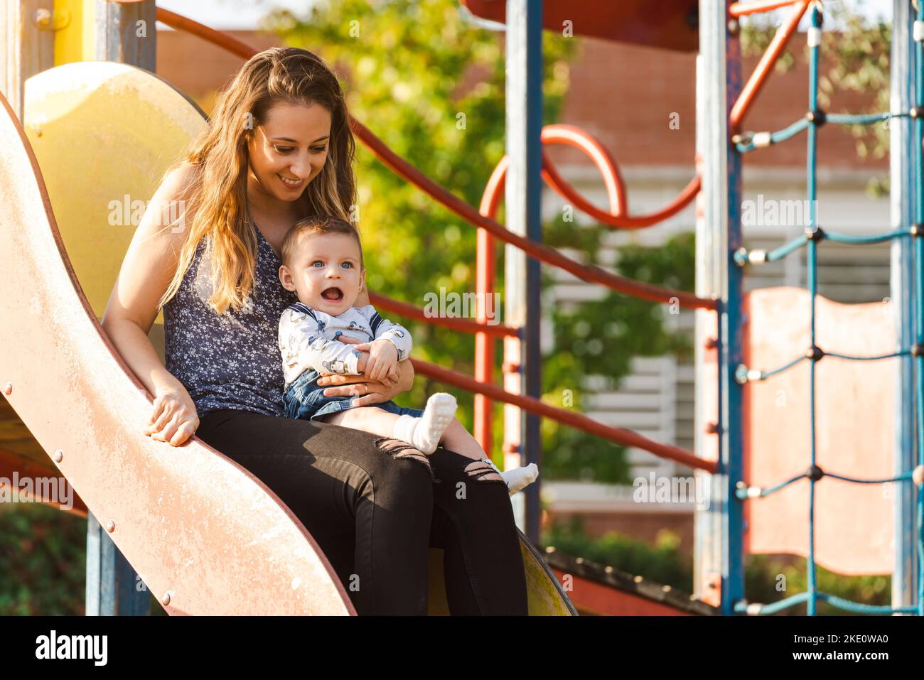 Madre con il suo bambino su uno scivolo del parco mentre il sole tramonta Foto Stock