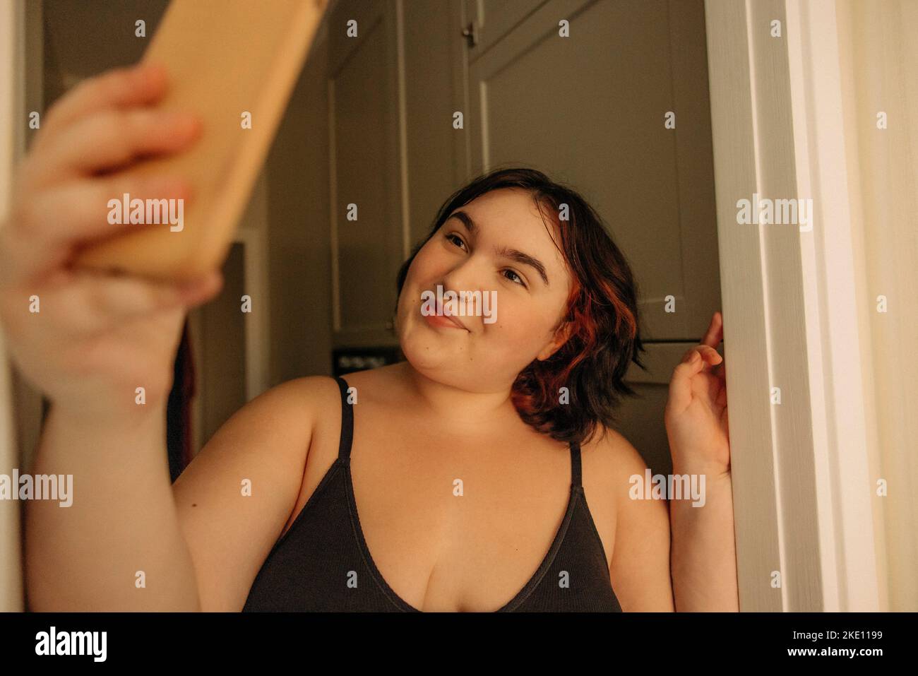 Giovane donna sorridente che porta il selfie attraverso il telefono cellulare a casa Foto Stock