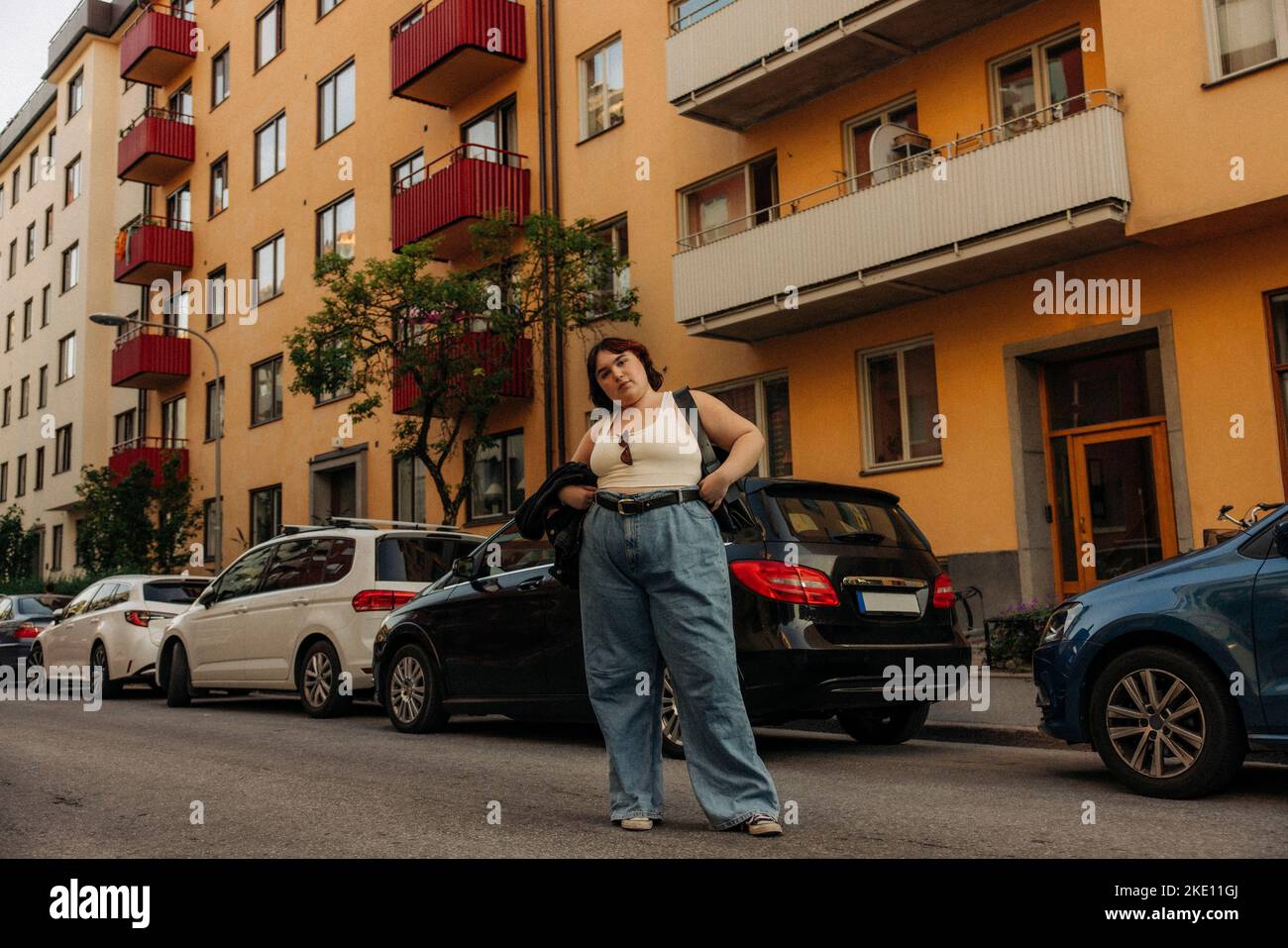 Ritratto di giovane donna fiduciosa in piedi con mano sull'anca contro le automobili Foto Stock