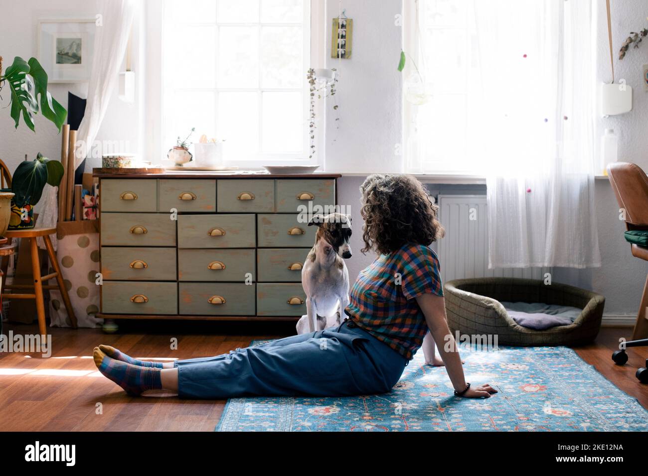 Vista laterale della donna seduta sul pavimento con cane a casa Foto Stock