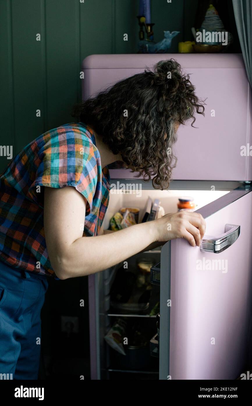 Vista laterale della donna che apre la porta del frigorifero in cucina Foto Stock