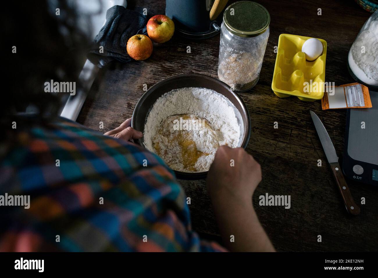 Vista ad angolo alto della donna che mescola l'ingrediente nella farina sul banco della cucina Foto Stock
