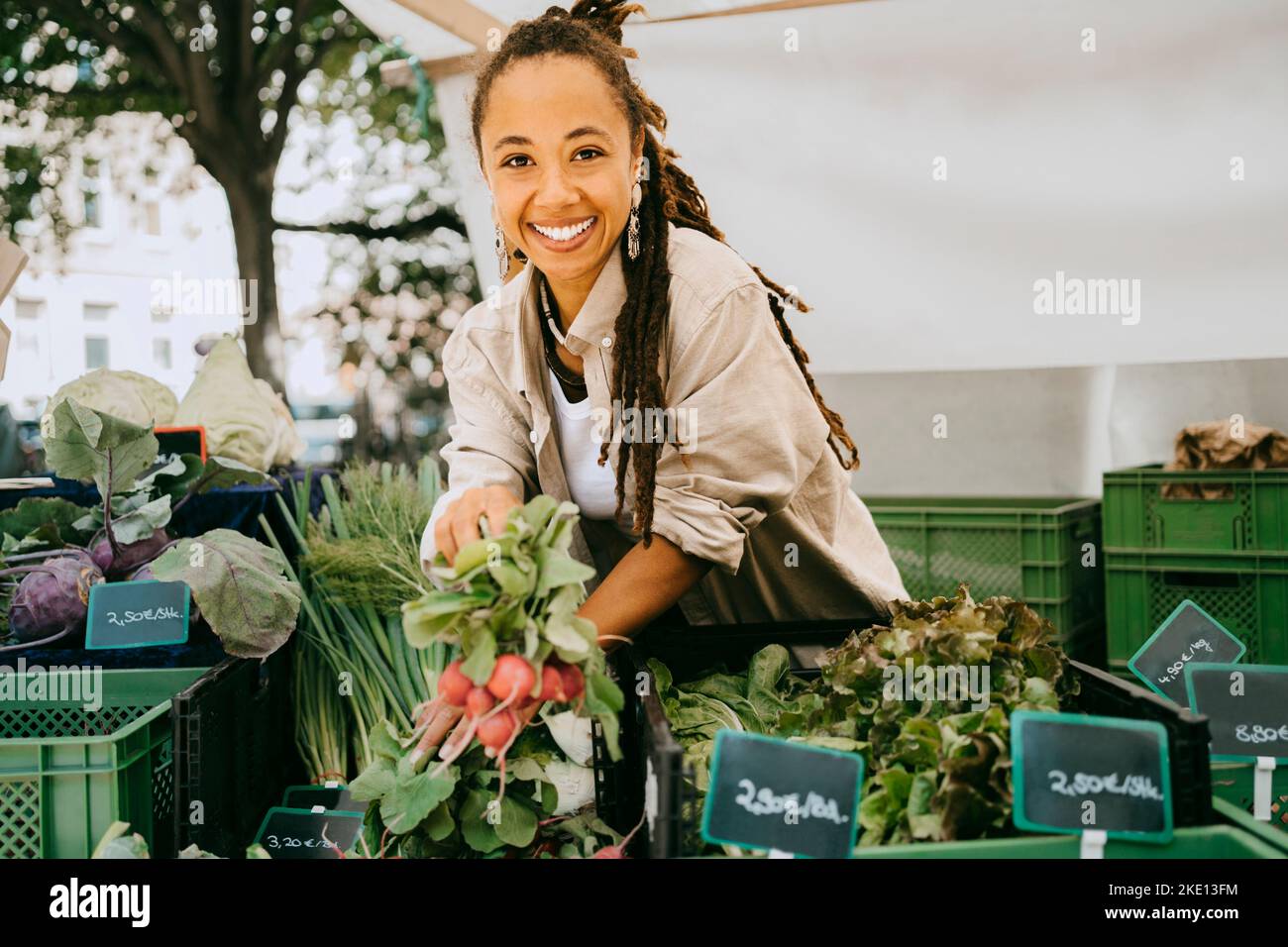 Ritratto di felice proprietario femmina che tiene verdure vicino alle casse in stalla al mercato Foto Stock