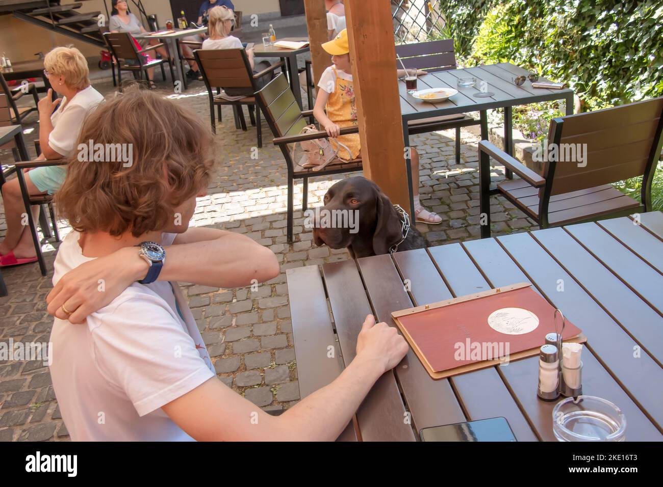 Bojnice, Slovacchia - 06.11.2022: Un giovane si siede a un tavolo in un bar e guarda il suo cane con piacere. Foto Stock