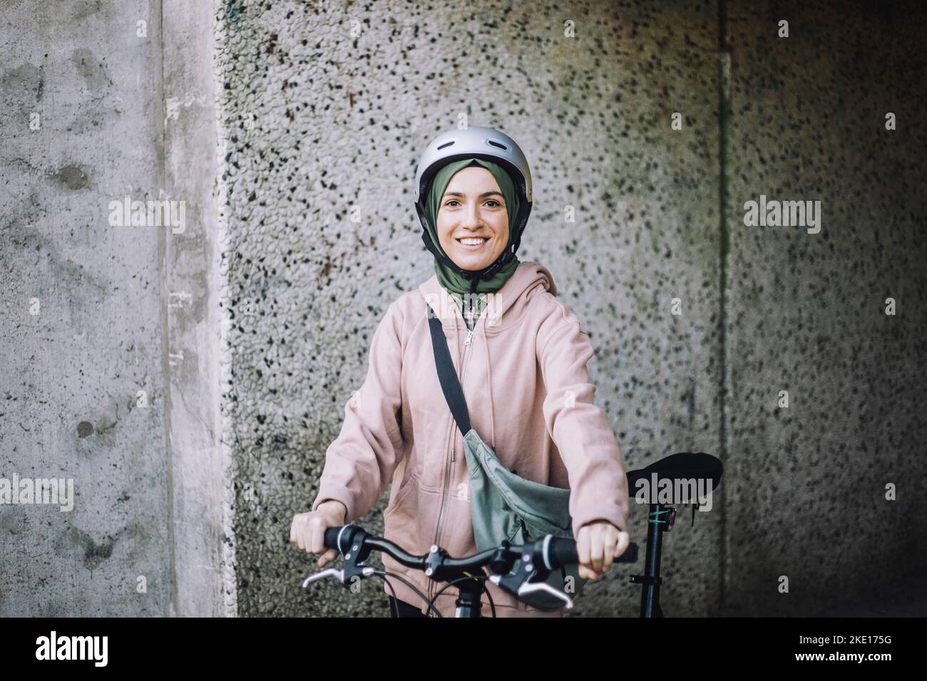 Ritratto di giovane donna sorridente con ciclo in piedi vicino al muro Foto Stock