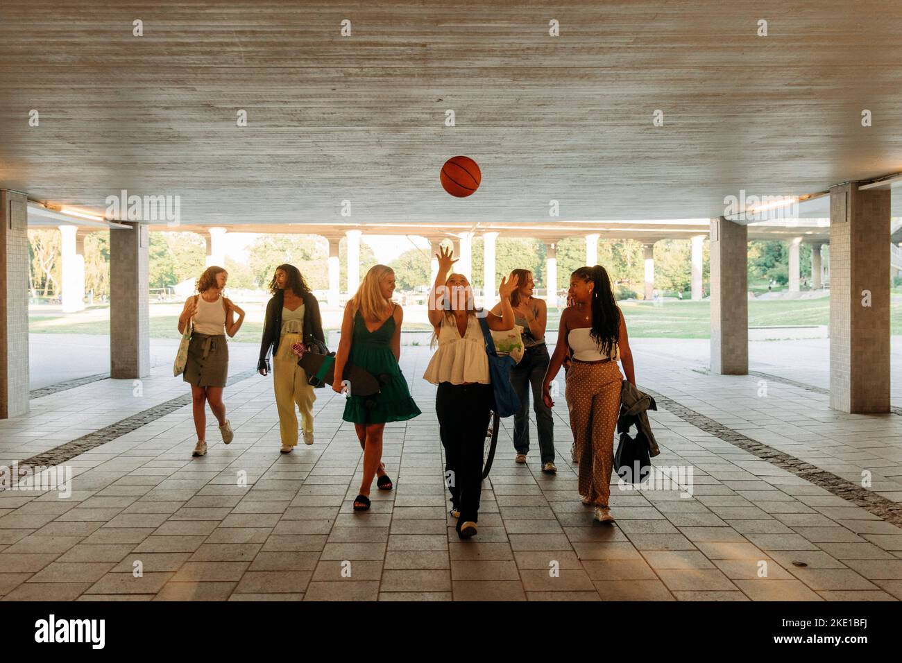 Ragazza adolescente che lancia il basket mentre cammina con le amiche sotto il ponte Foto Stock