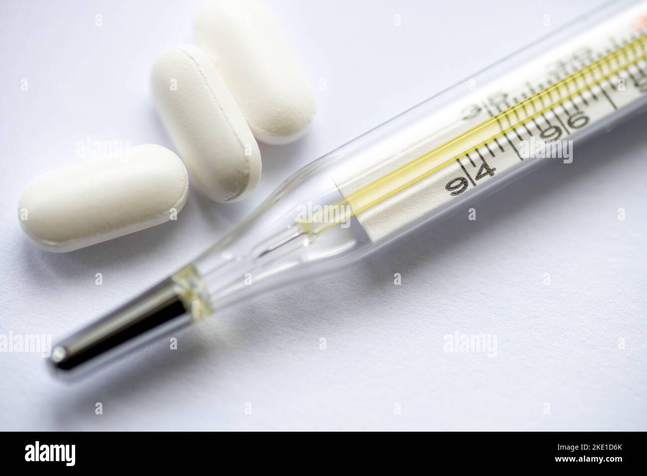 Primo piano di un termometro analogico con alcune compresse di medicinali isolate su sfondo bianco. Foto Stock