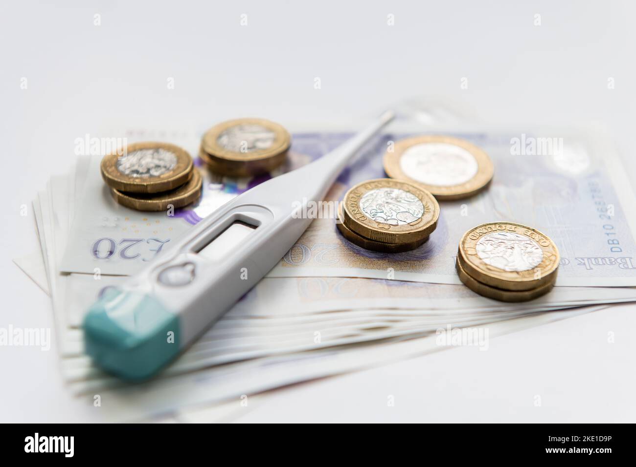 Un concetto di costo per l'assistenza sanitaria con termometro digitale e monete in cima a un mucchio di banconote isolate su sfondo bianco. Foto Stock