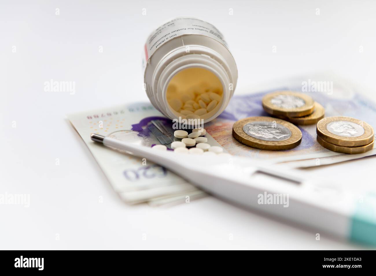 Un concetto di costo per l'assistenza sanitaria con una bottiglia di medicinale, un termometro e monete in cima alle banconote isolate su sfondo bianco. Foto Stock