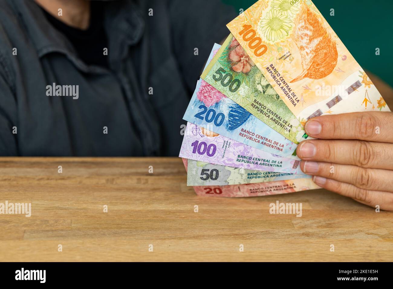 L'uomo dietro la scrivania sta tenendo un pacco di pesos argentini, banconote varie Foto Stock