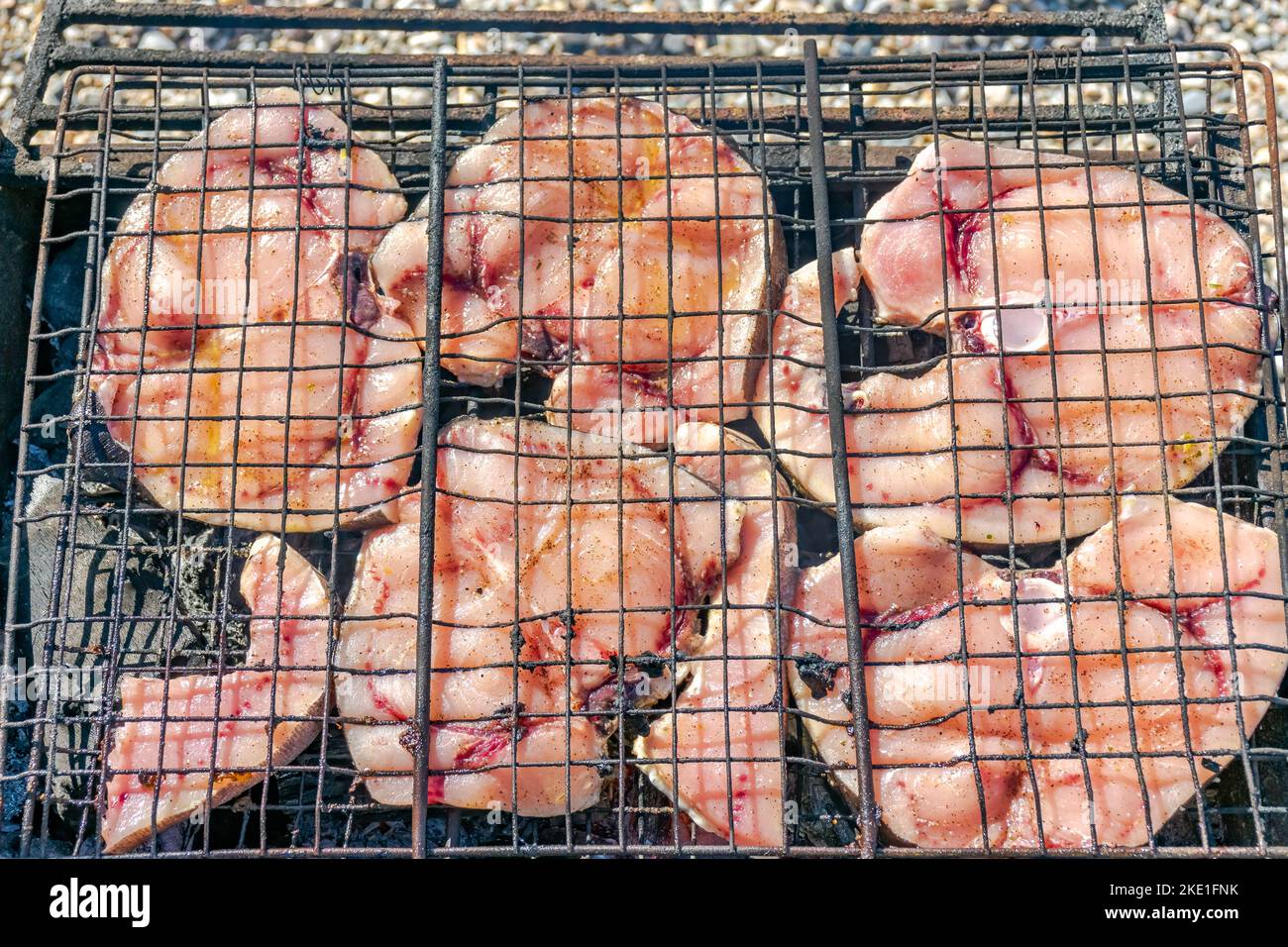 Vista dall'alto di fette di pesce spada grigliate in un barbecue con ciottoli di spiaggia sfocati sullo sfondo. Foto Stock