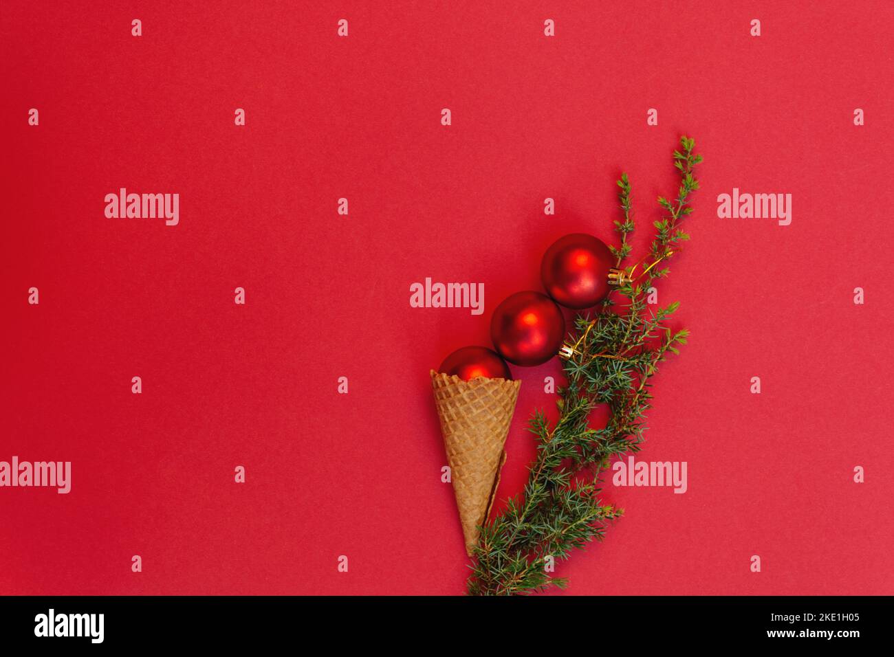 Tre giocattoli rotondi in gustoso cono waffle e accanto ad esso ramo verde dell'albero di Natale su sfondo rosso. Concetto di celebrare le fredde vacanze invernali in calore. Vista dall'alto, disposizione piatta. Copia spazio Foto Stock