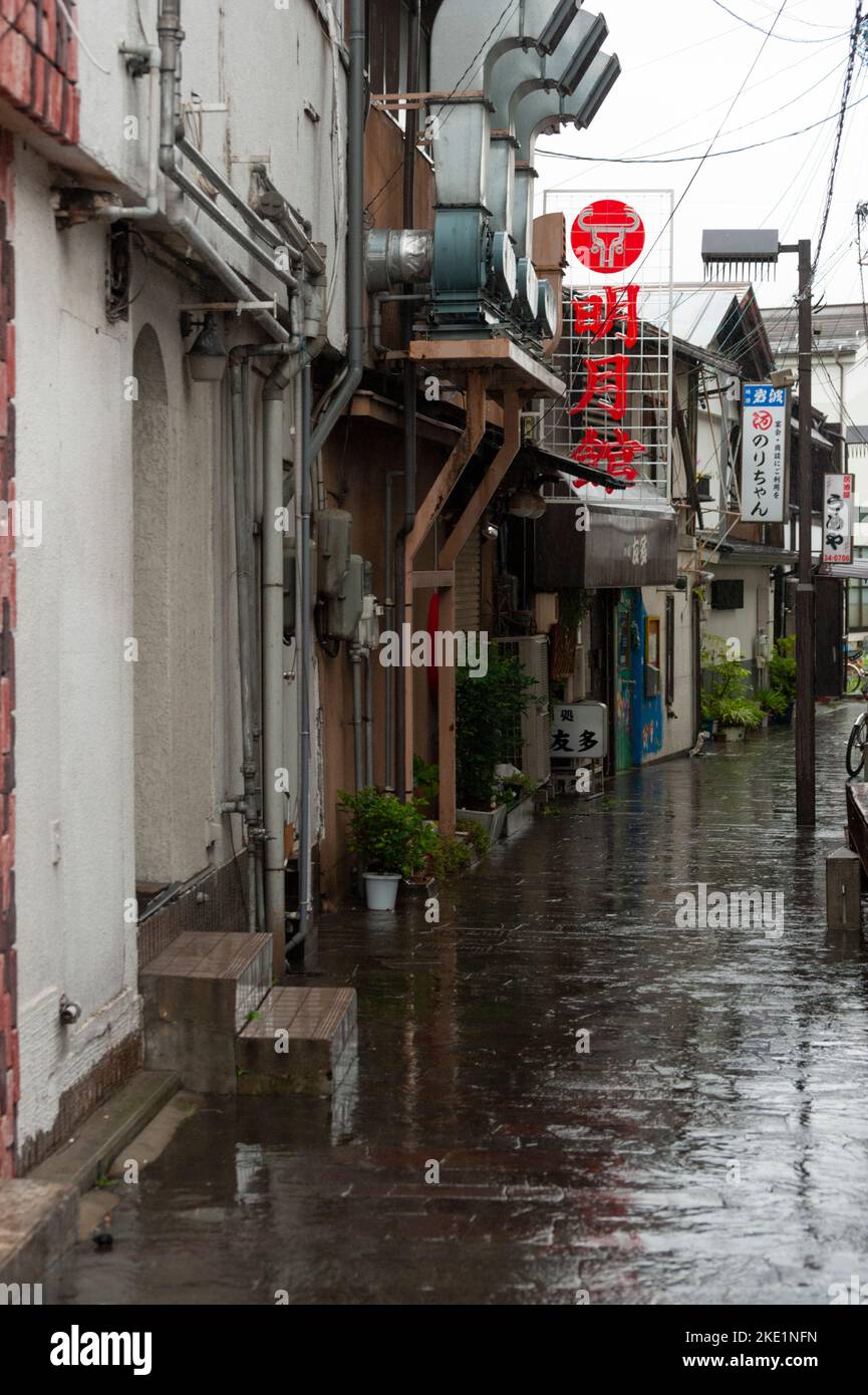 Un piccolo bar locale e locali dove bere si trovano lungo una strada stretta a Matsumoto in una giornata piovosa. Foto Stock