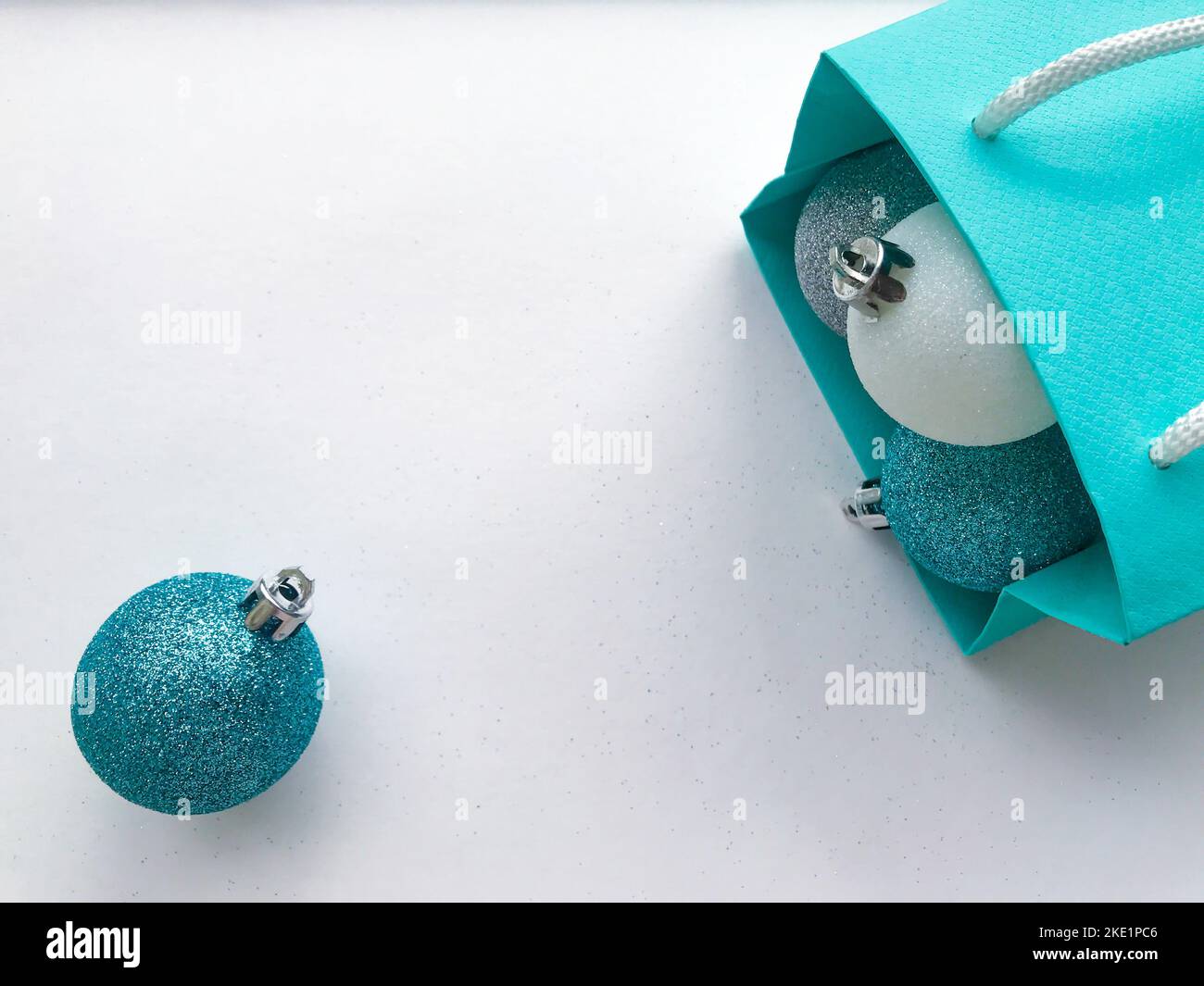 Borsa regalo in carta blu turchese, all'interno della quale sono visibili palline di Natale lucenti di colore blu, argento e bianco. Una palla turchese rotolata via e. Foto Stock