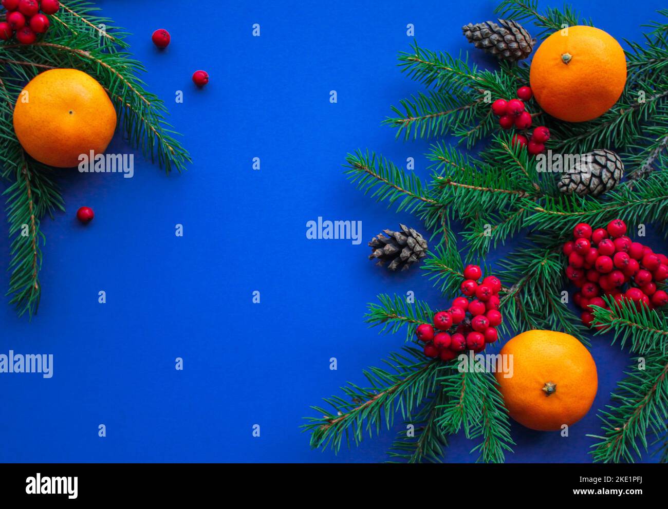 Lo spirito del Natale: Rami di abete, coni, bacche di rowan rosso brillante e tangerini arancioni su uno sfondo blu scuro luminoso con spazio per il testo Foto Stock