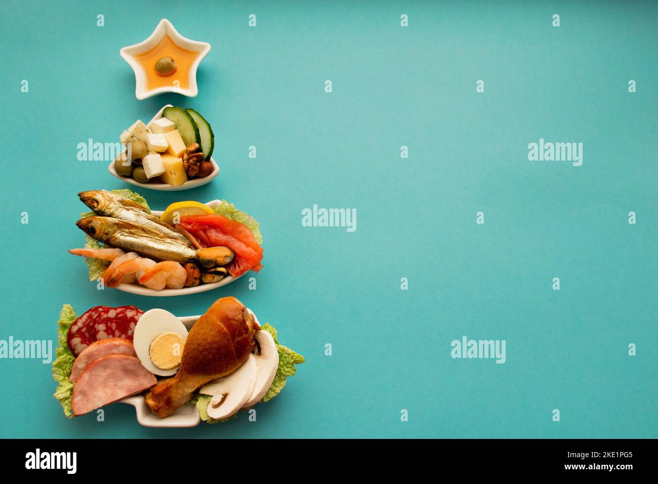 Piatto in forma di albero di Natale con cibo proteico - carne, pesce, formaggi, noci, ecc sfondo blu. Il concetto di dieta del cheto tratta per l'hol Foto Stock