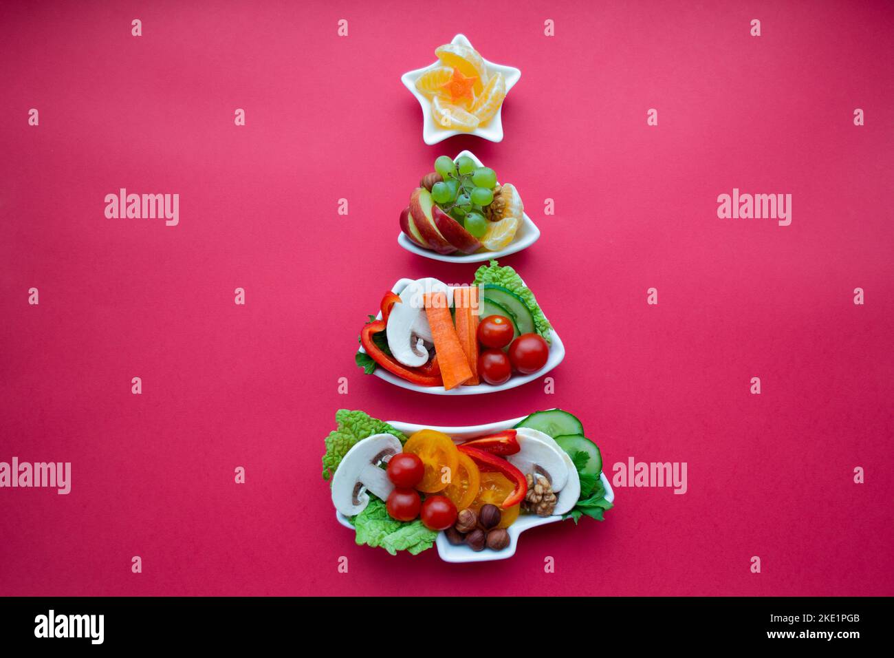Piatto in forma di albero di Natale con verdure, frutta, funghi e bacche. Sfondo rosso. Il concetto di prelibatezze vegetariane per le vacanze Foto Stock