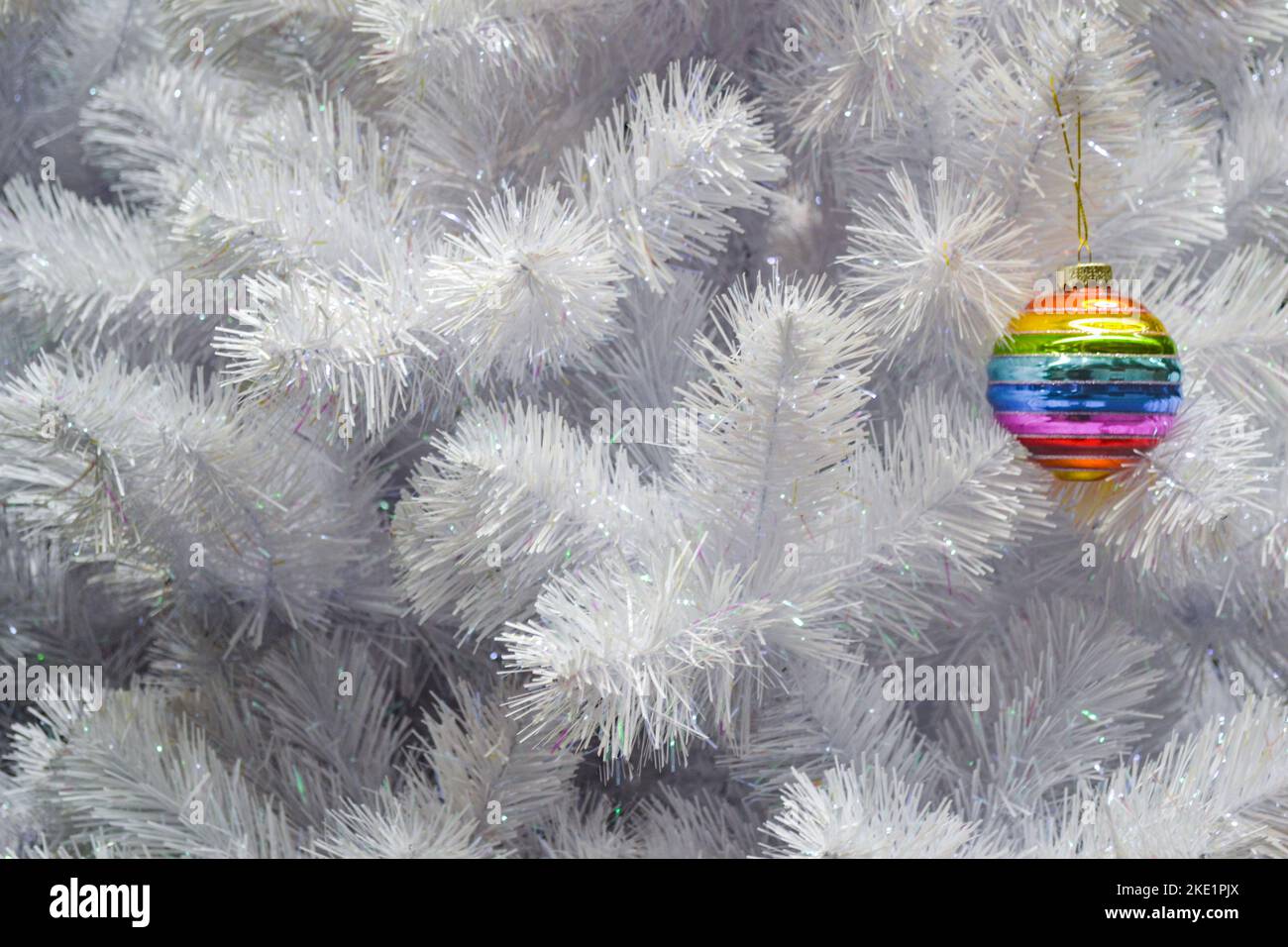 Sfera di Natale colorata arcobaleno di vetro luminoso, bauble appeso su un albero di natale artificiale bianco. Il concetto della festa, Natale, simbolo del Foto Stock