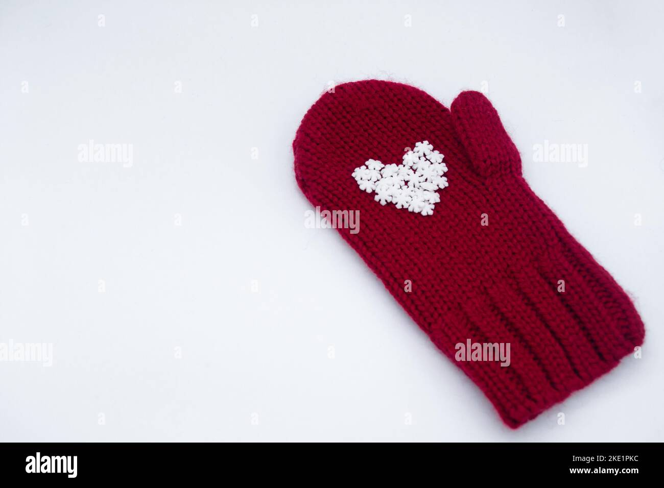 Un mitten rosso lavorato a maglia, su cui si trovano fiocchi di neve bianchi a forma di cuore come nel palmo della mano su uno sfondo bianco, isolato. ?oncept di Foto Stock
