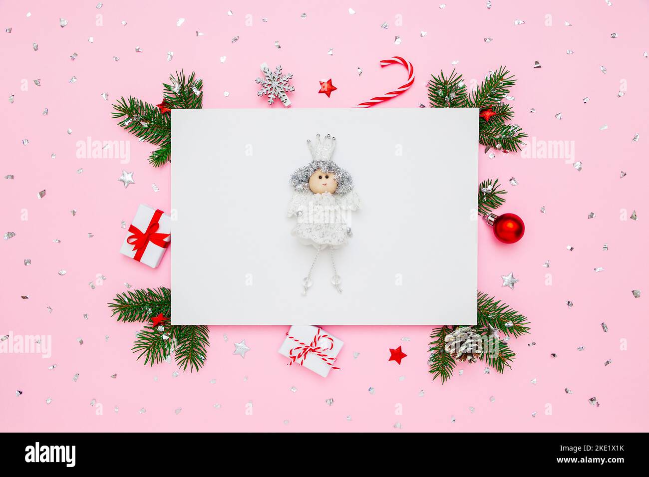 Biglietto di Natale con spazio per la copia. Principessa su carta bianca in cornice di rami di abete naturale, regali e decorazioni su piatto rosa pastello Lay bac Foto Stock