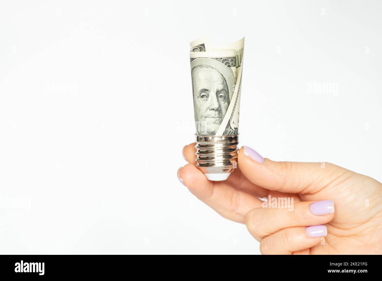 La mano di una donna tiene una cartuccia da una lampadina con dollari su uno sfondo bianco, il prezzo dell'elettricità, la tecnologia Foto Stock