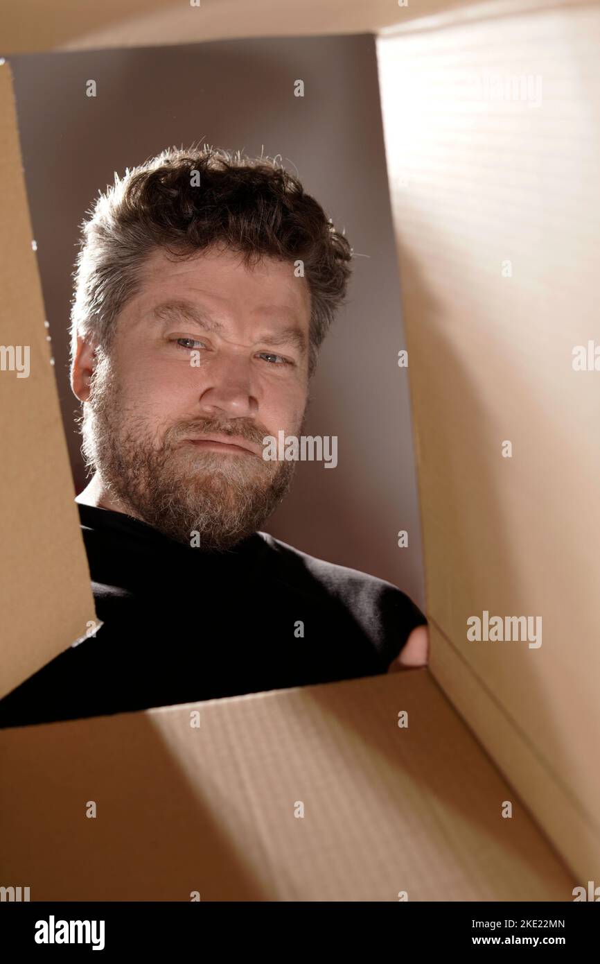 uomo barbuto che guarda all'interno di una scatola con uno sguardo infelice sul suo volto Foto Stock