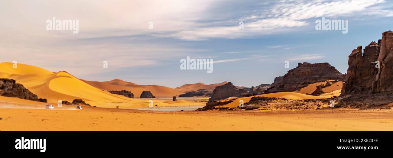Vista panoramica sulla duna di sabbia del deserto del Sahara e sulle montagne rocciose di Tadrart Rouge, Djanet, Illizi. Far 4WD veicoli fuoristrada che attraversano la polvere di erg Foto Stock