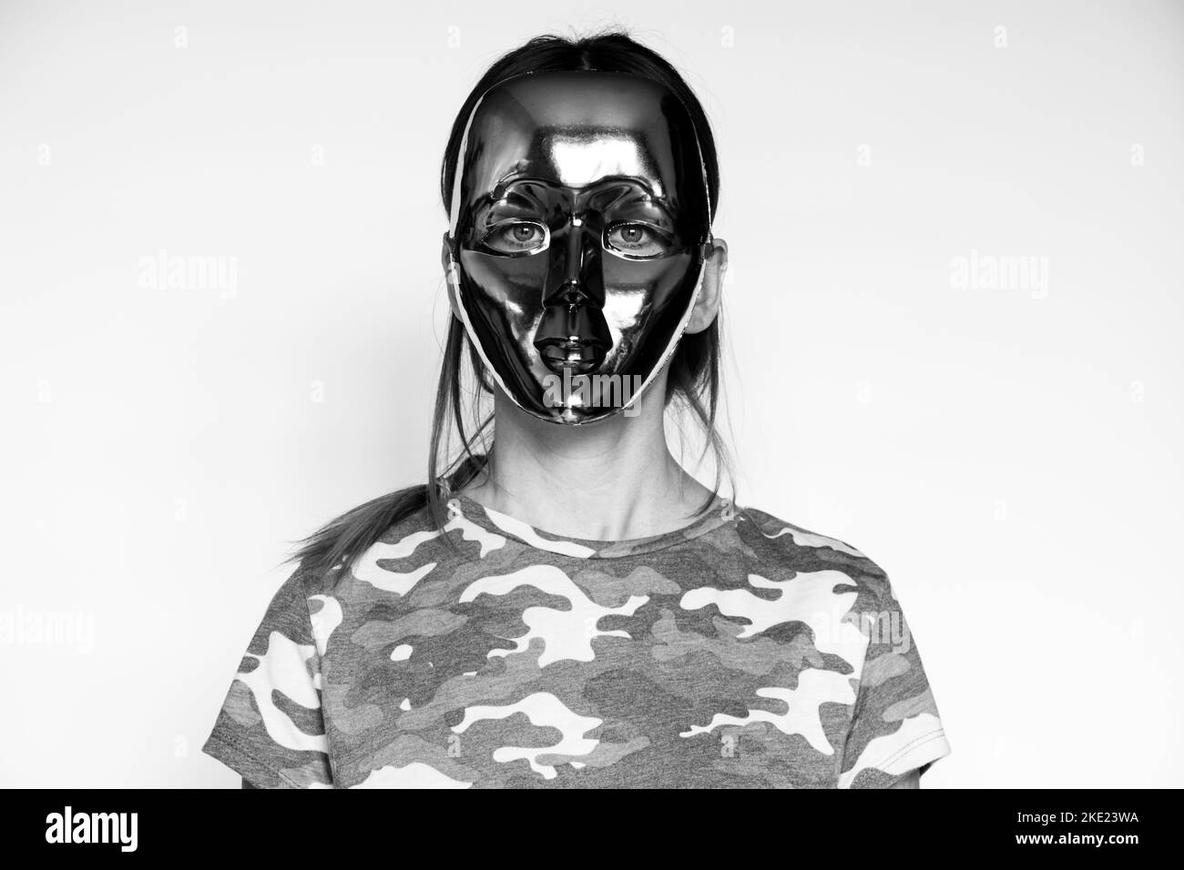 Una ragazza militare in una maglietta mimetica e una maschera senza volto su sfondo bianco, una ragazza militare Foto Stock