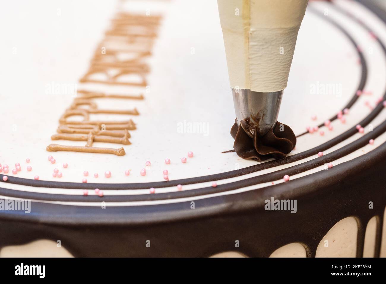 Decorazione di una torta bianca di compleanno con glassa al cioccolato Foto Stock