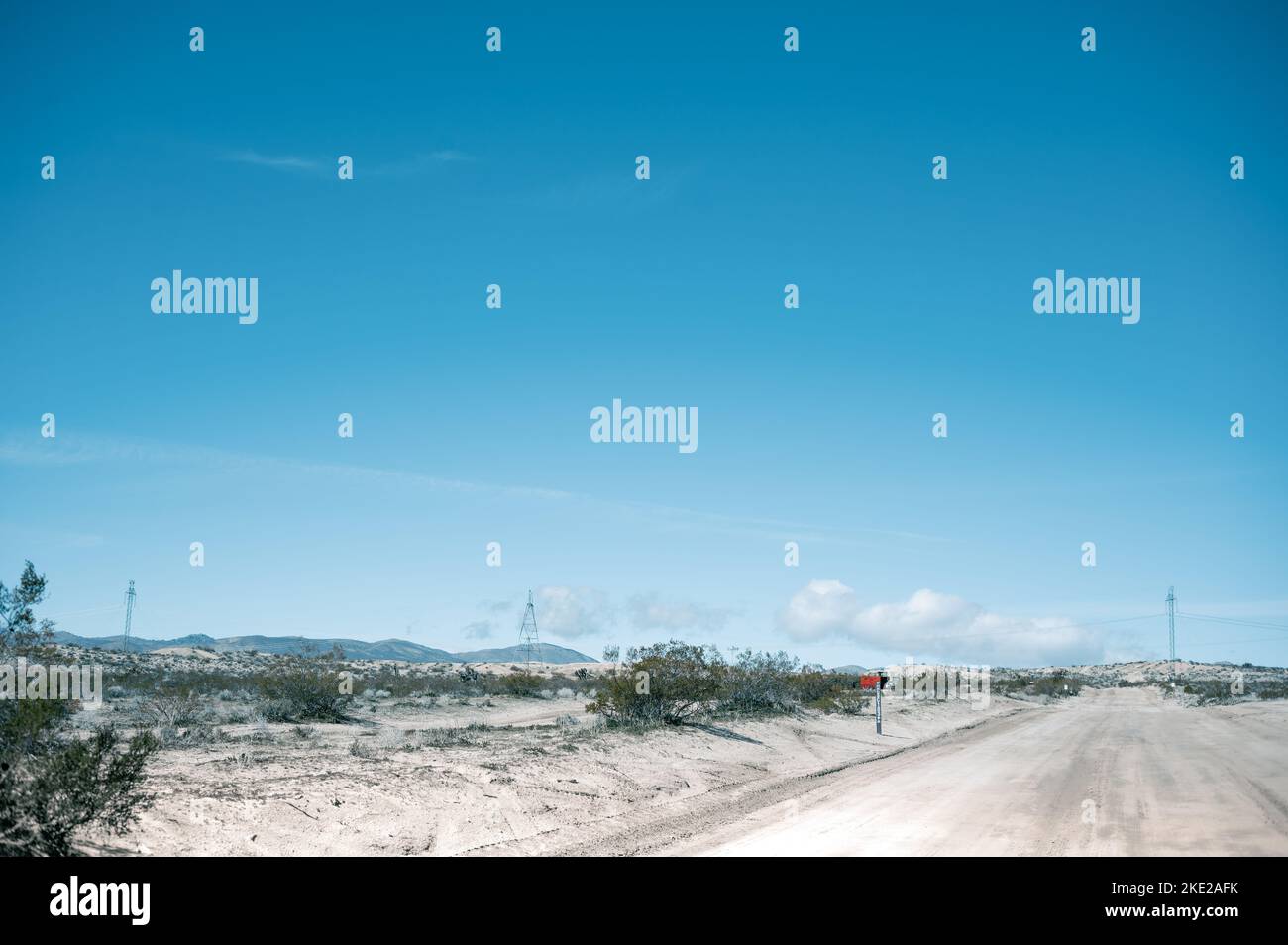 Strada sterrata nel deserto del Mojave con linee elettriche che attraversano lo sfondo e le montagne all'orizzonte Foto Stock