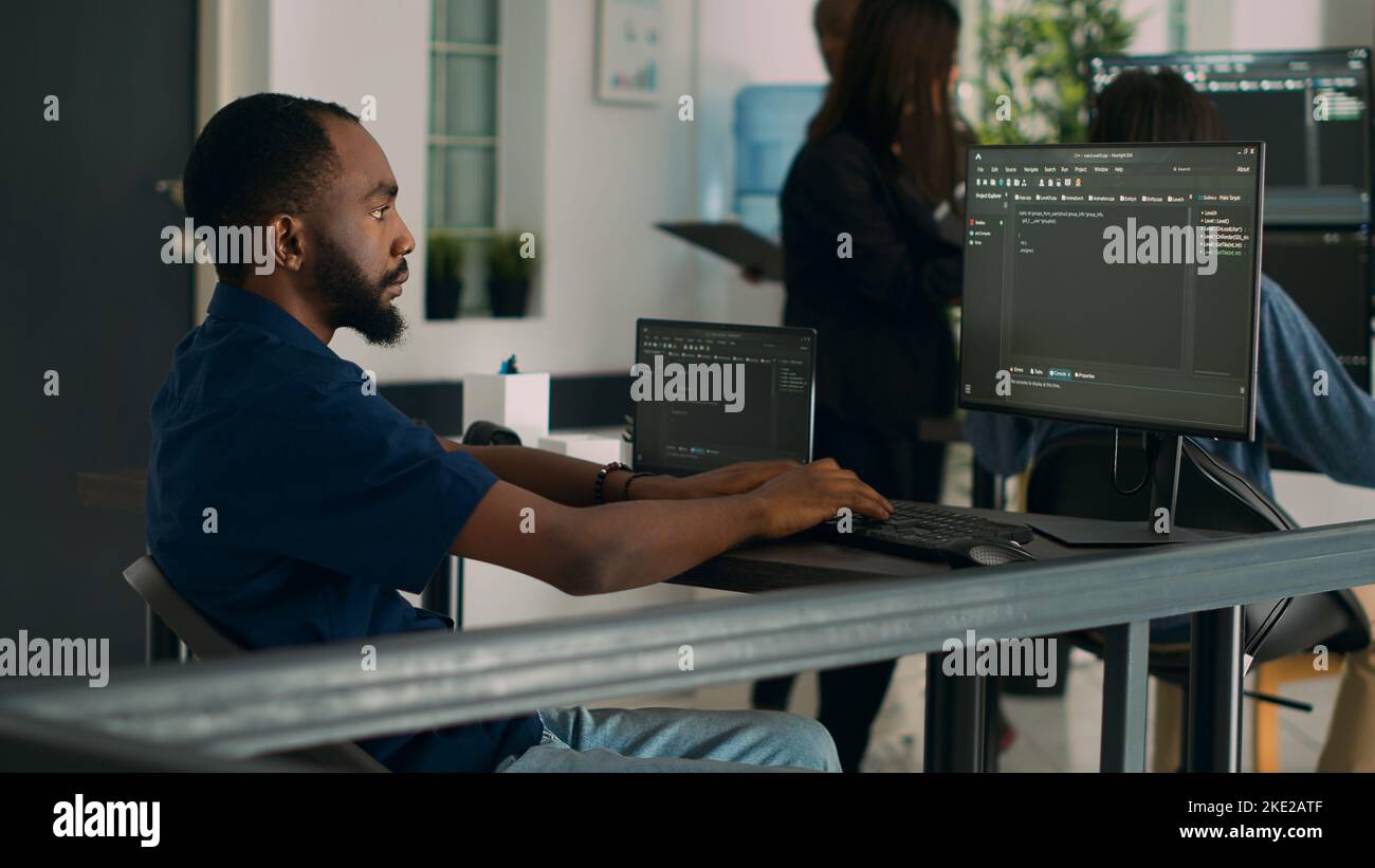 Codificatore afroamericano che sviluppa l'interfaccia dell'applicazione con il codice e lo scritto del HTML sulla finestra del terminale, programmarlo il linguaggio. Sistema di egineer utilizzando le informazioni del database in agenzia di sviluppo. Foto Stock