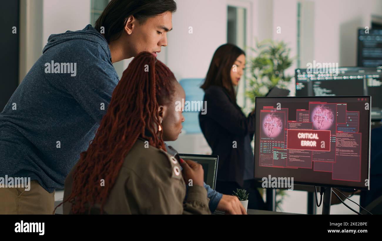 Team eterogeneo di amministratori di database che hanno violato il server e l'avviso di violazione della sicurezza sul computer, cercando di risolvere il problema dell'hacking. Si è verificato un messaggio di errore critico lampeggiante sullo schermo. Foto Stock