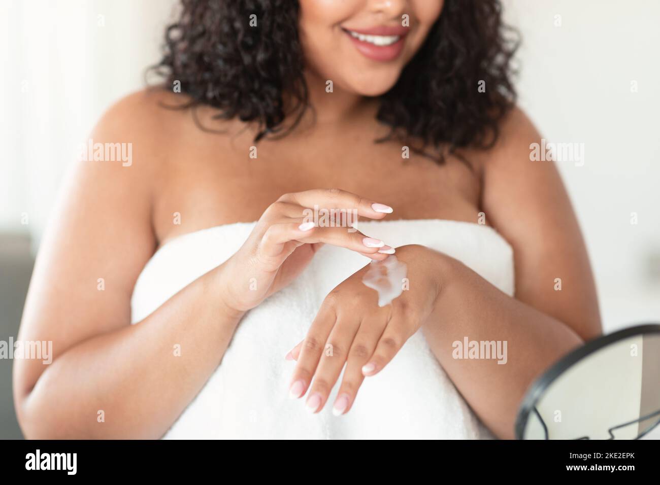 Colpo di primo piano di nero più taglia donna applicando crema idratante sulle mani, utilizzando lozione nutriente per la pelle secca Foto Stock