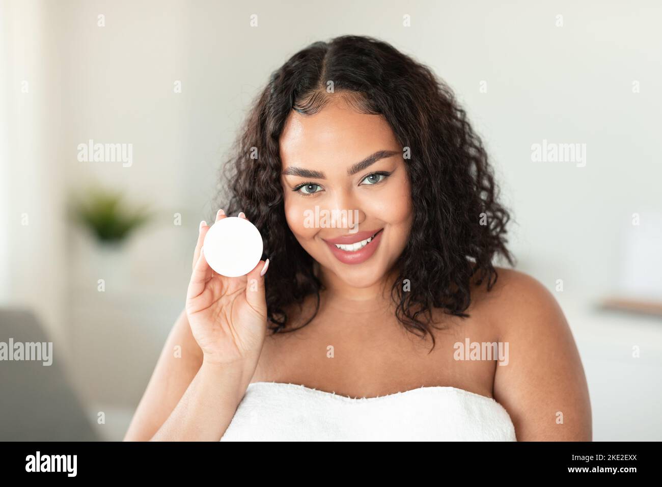 Trattamenti per la pelle. Felice ragazza cubby afro-americana che tiene aperto il vaso con crema e sorridente alla macchina fotografica Foto Stock